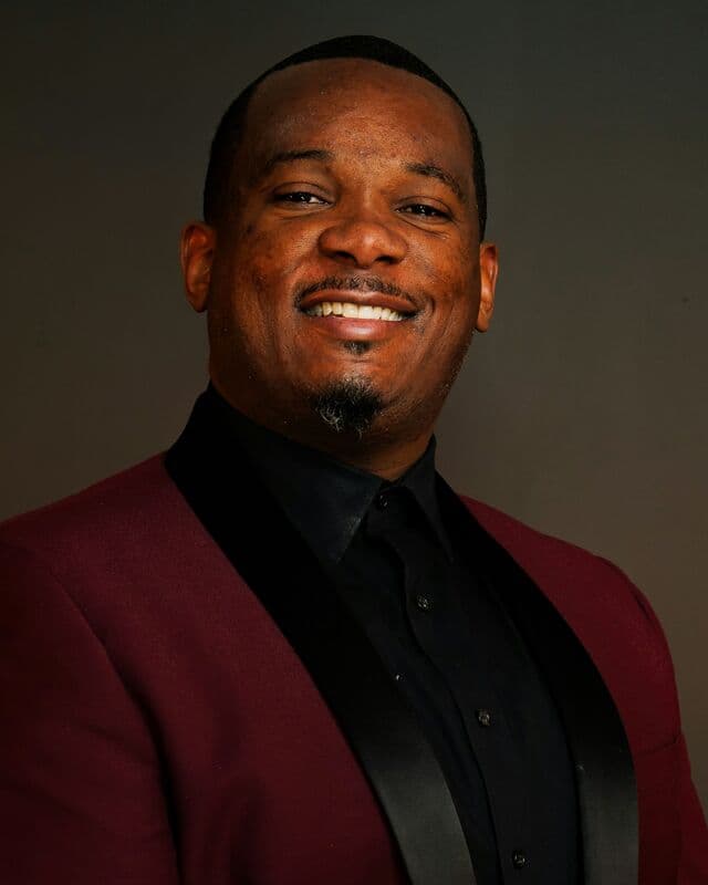 A smiling man in a maroon suit